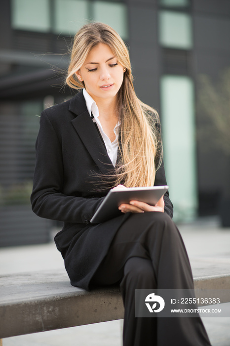 Detail of a businesswoman using her tablet while sitting on a bench in a city