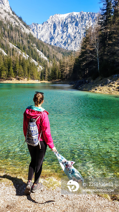 Woman enjoying a peaceful Green Lake, located in an Alpine valley in Austria. The algae in the lake give it its distinctive color. Lots of pine trees on the shore. The girl is holding a silky scarf