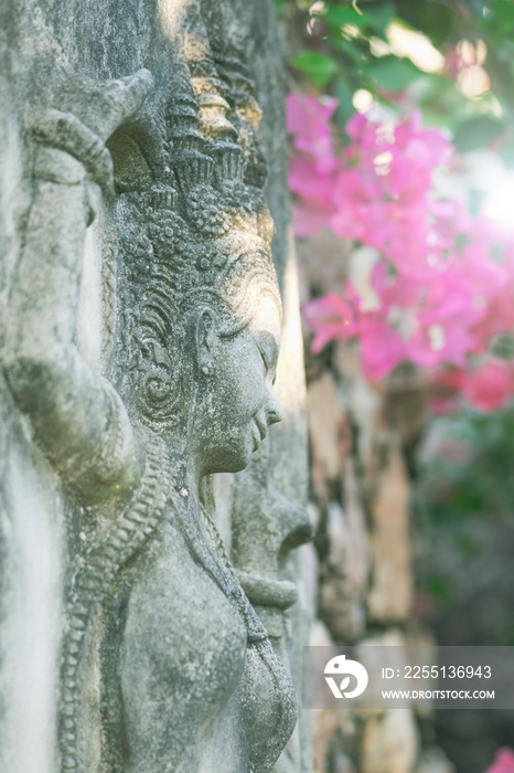 Abstract background of ancient woman stone decoration in pink flower blossoms background illuminated by sun beams in Thailand. Image with shallow depth of field