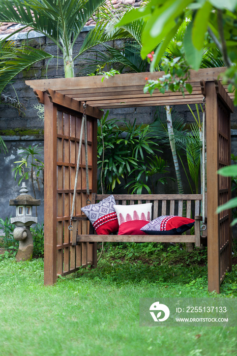 Classic outdoor wooden swing in the green garden with pillows