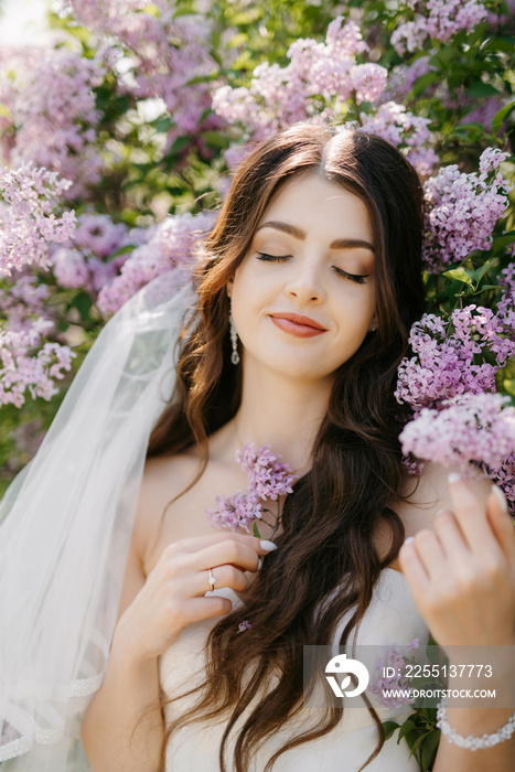 young girl bride in a white dress in a spring forest in lilac bushes