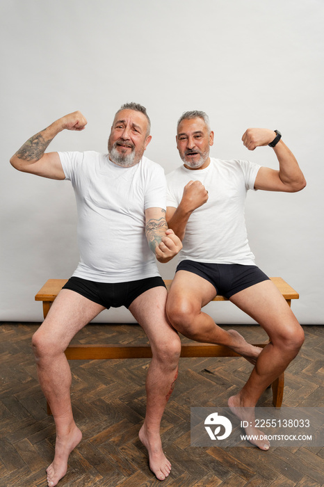 Portrait of two men flexing muscles against gray background