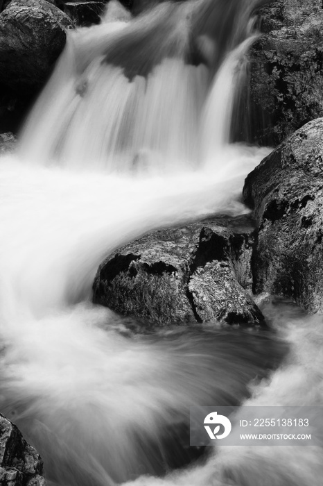 river rocks in smooth satin water flow of waterfall in black and white in long exposure