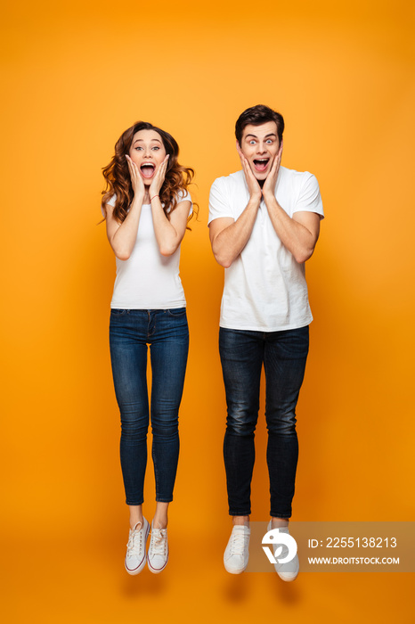 Full-length photo of amusing man and woman in casual posing together while jumping with hands on face, isolated over yellow background