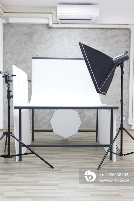 Indoor with air conditioner studio white photoshoot scene table and partition with professional photographer equipment softbox strobe flash reflector light on tripod stand ready for shoot products