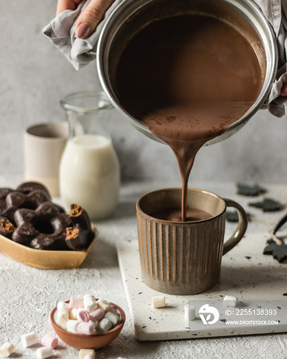 Cup of hot chocolate poured on bright background with cookies and marshmllow