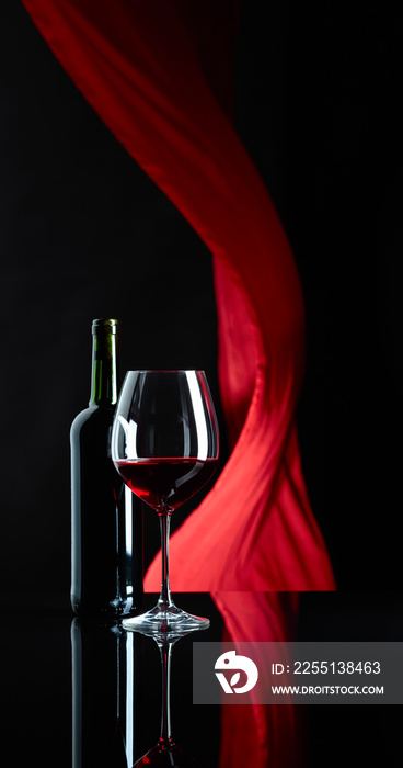 Wineglass and bottle of red wine on a black reflective background.