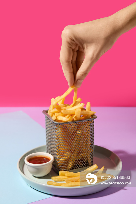 Female hand with tasty french fries on color background