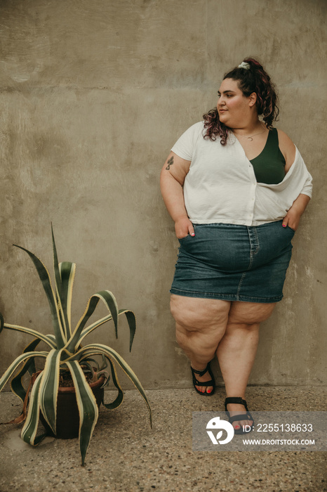 plus size woman stands against textured wall next to plant