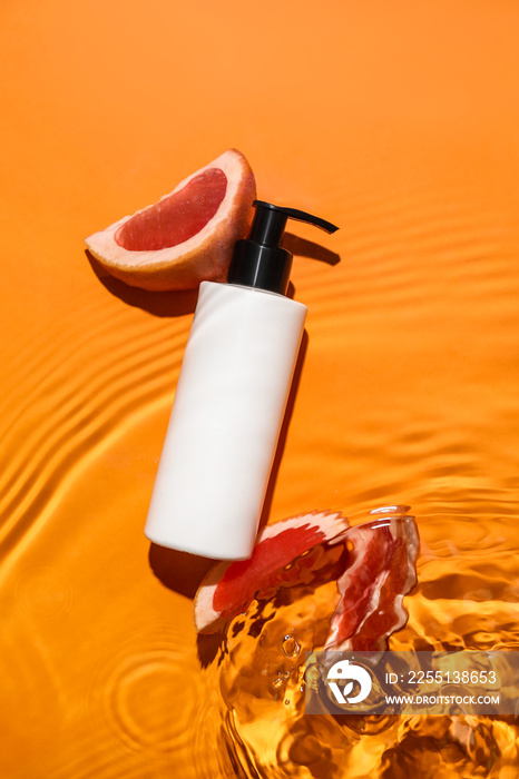 Bottle of cosmetic product and cut grapefruit in water on color background