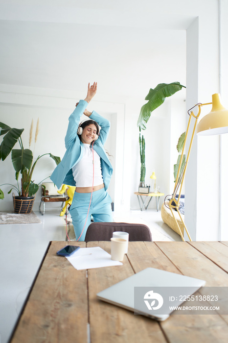 Successful Latina businesswoman dances in office attire happily celebrating at work. Female office worker with headphones doing the crazy in the workplace.