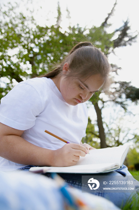 Young mid-sized woman with Down Syndrome writing in journal outdoors