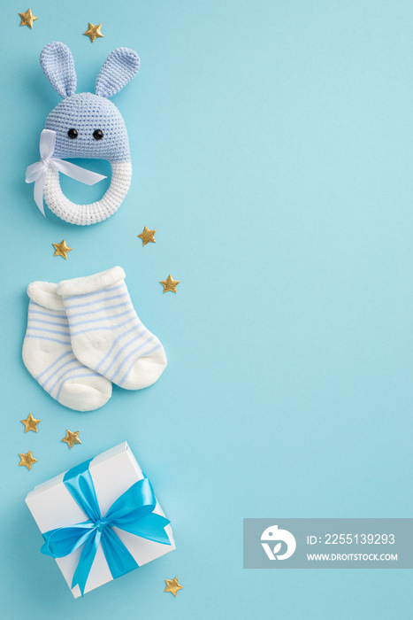Baby boy concept. Top view vertical photo of gift box socks knitted rattle bunny toy and gold stars on isolated pastel blue background with copyspace