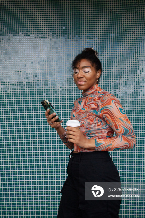 Young curvy woman with vitiligo looking at her phone in front of tiled wall