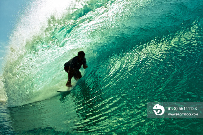 Surfer silhouette riding wave inside the tube barrel