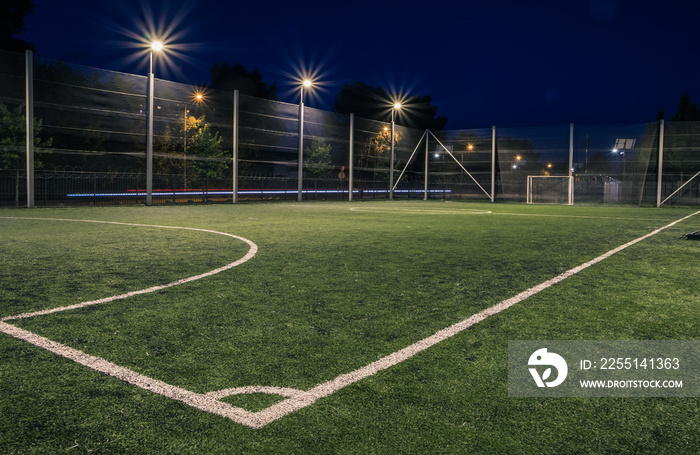 An amateur soccer field illuminated at night. A small football field lit by lanterns in the evening. Green football field illuminated at night. Soccer field in night with spotlight