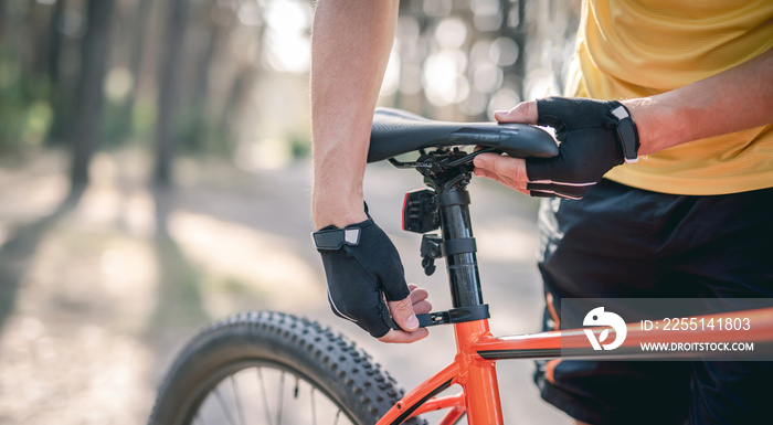 Rider adjusting seat height on bicycle standing in sunny forest