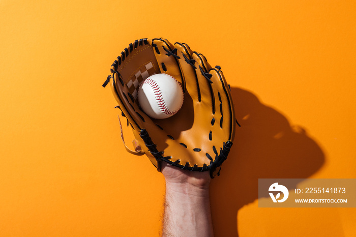 cropped view of man holding softball in brown baseball glove on yellow