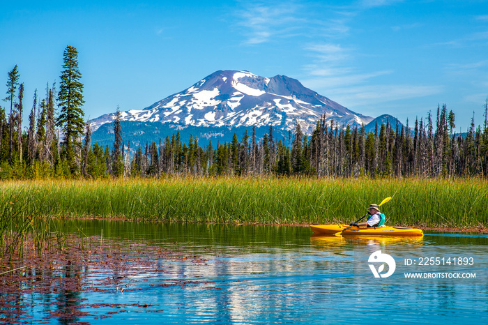 Bend, Oregon;  Hosmer Lake in central oregon, with the south sister reflected in the lake and a man in a kayak paddling by.