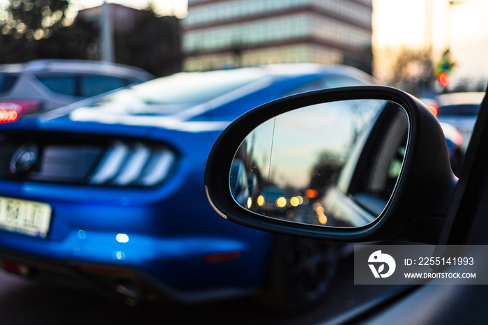 Traffic seen thru a car mirror and a Mustang in the background at sunset