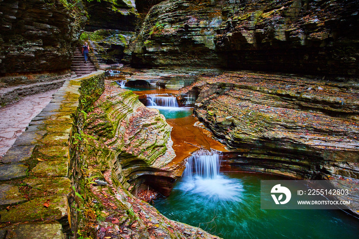 Fall foliage covering terraced rocks in gorge with stone path and stunning blue waterfalls cascading through river