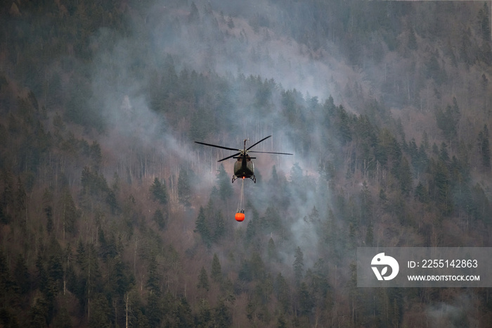 The helicopter carrying a bucket to deliver water for aerial firefighting in a mountain forest