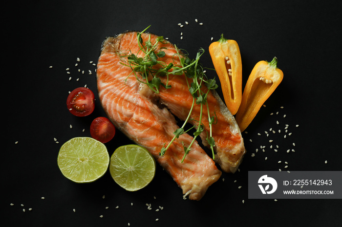 Tasty grilled salmon and ingredients on black background