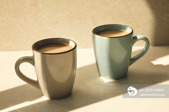 Two cups of coffee on a beige stone background with shadows and reflections. Front view