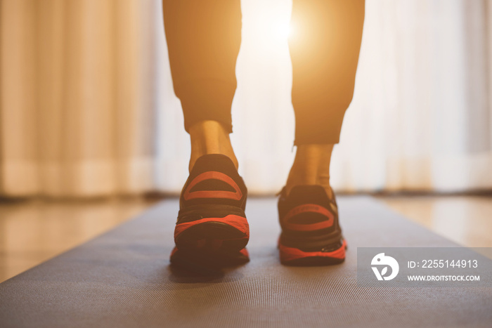 A young athlete, wearing jogger pants and black sneakers, stands on a gym mat getting ready to work out at home in the morning.