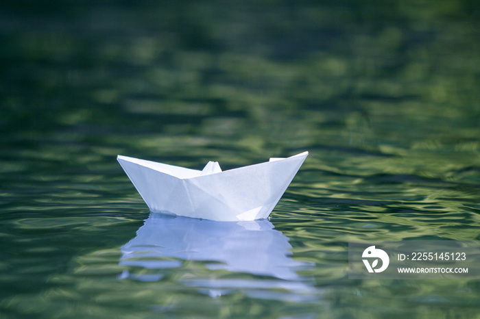 Close-up of simple small white origami paper boat floating quietly in blue clear river or sea water under bright summer sky. Freedom, dreams and fantasies concept, copyspace background.