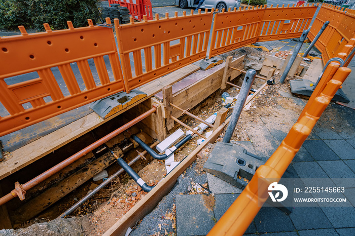 Excavation on a city street to replace plastic water pipes or laying cables. Repair and renovation at construction and development site. Fence for safety of pedestrians and cars.