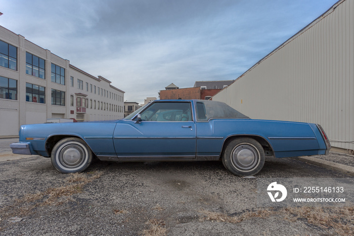 Long blue seventies style car parked in urban industrial area