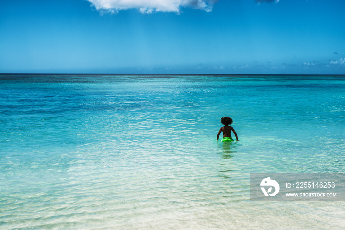 Young african boy standing in crystal clear water on tropical island.