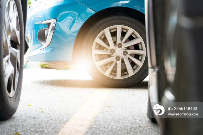 Luxury blue car parked in garage. There are blurry images of two cars in the front. Sunlight shines from the back through the wheel.