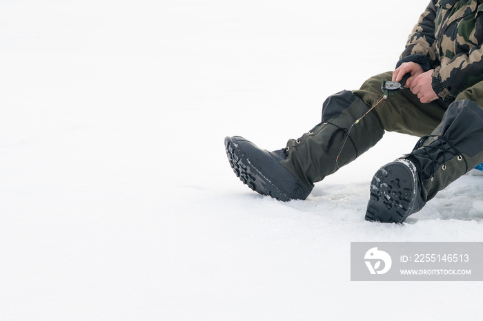 Winter fishing on ice. Man jiggling bait in an ice hole. Relaxing in the wild