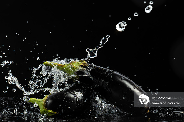 Eggplant on a black background with drops and splashes of water