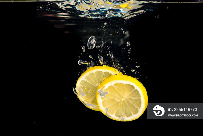 Slices of lemon thrown into water on a black background