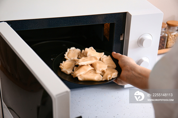 Woman putting plate with food in microwave oven