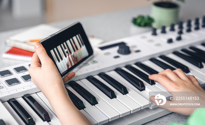 The child learns to play the piano with a smartphone, online music lesson.