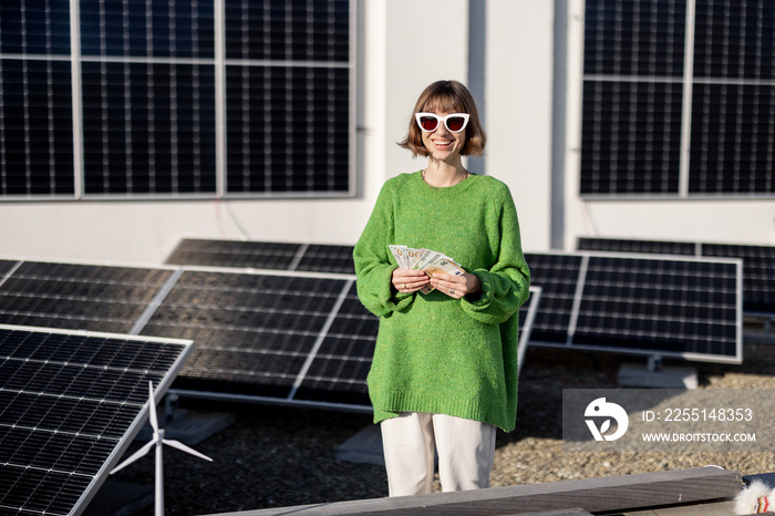 Woman counts dollar banknotes saved due to the generation of energy from a solar power plant installed on her house rooftop. Concept of investment in alternative energy