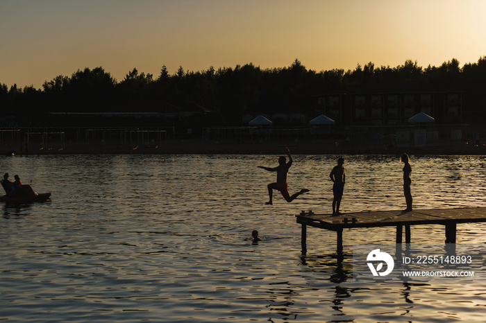 People jump from the pier into lake Issyk Kul. Guys swim in the lake at sunset. The texture of the surface of the water. Rest in Kyrgyzstan.