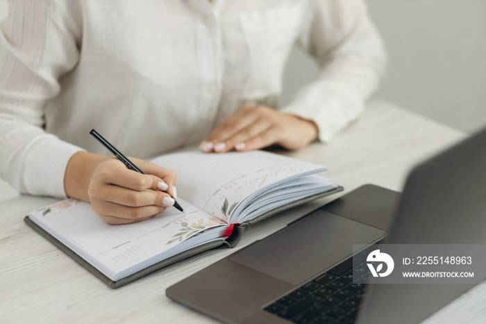 Young teacher works at the computer. She writes in her notebook