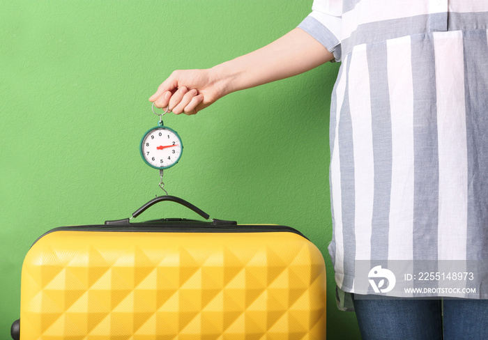 Woman weighting heavy luggage on color background