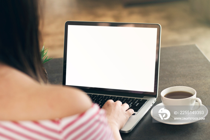 Mockup image of a woman using laptop with blank white screen on wooden table in cafe