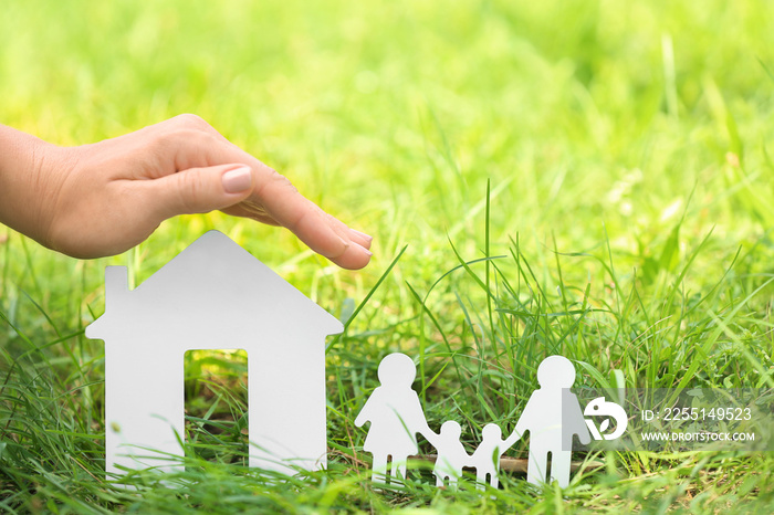 Woman holding hand over figure of wooden house and family on green grass