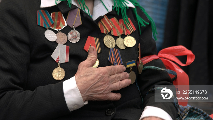 War veteran with hand over heart and awards. Orders and medals on female veteran chest. Celebration of Victory Day.