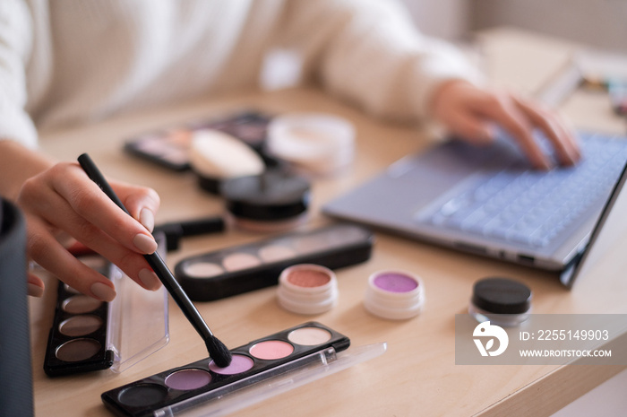 A faceless woman watches online training from a professional makeup artist on a laptop. Distance learning