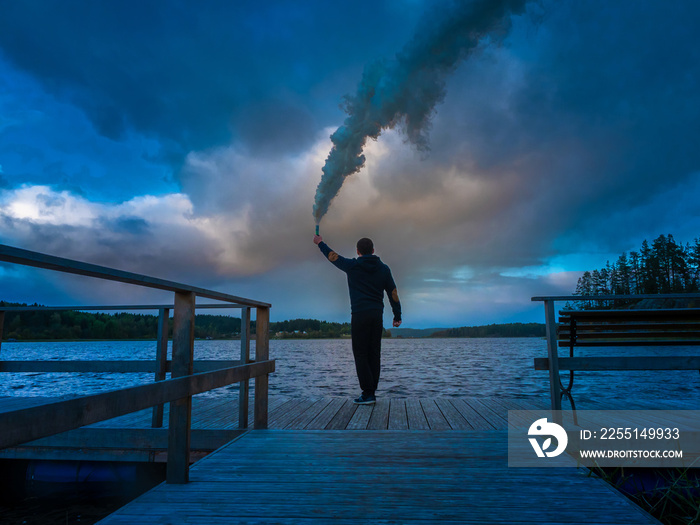 SOS signal. A man with a smoke bomb. A man gives a signal with smoke. Help. Silhouette of a man. The man calls the rescuers.