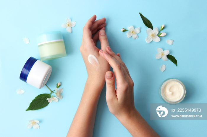 beautiful female hands and cosmetic cream and flowers on a colored background. To smear arms or hand with a cream, an elastic skin.