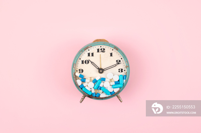 Old alarm clock with Tablets, medicine and pills on clock face on pink background. colorful capsules on  clock. Health care, reform, Take medicine on time concept